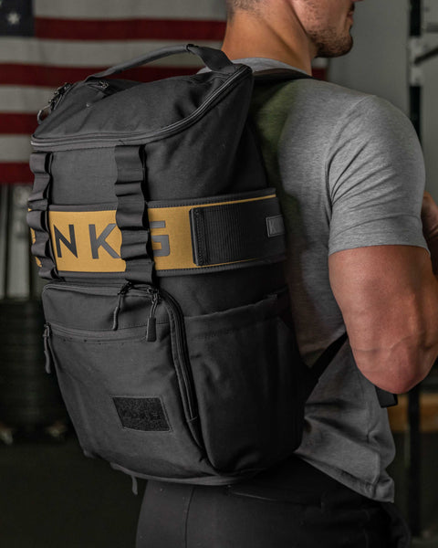 Man wearing large black CORE Backpack in gym, standing in front of American Flag