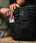 Person reaching for FITAID inside drink bottle pocket of KNKG Mini CORE Backpack in Black