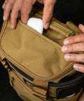 Top view of airpods being packed inside pocket of KNKG CORE Mini Backpack in Tan Desert color