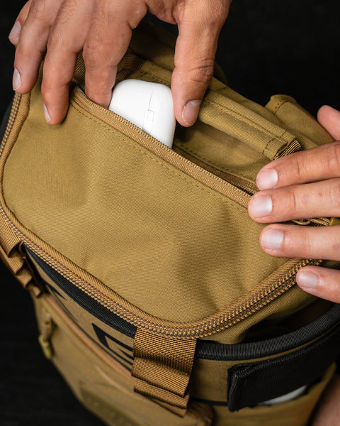 Top view of airpods being packed inside pocket of KNKG CORE Mini Backpack in Tan Desert color