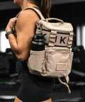 Person wearing neutral beige mini size KNKG CORE Backpack with a water bottle, blurred background