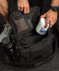 Person packing KNKG mini black CORE Duffel with a supplement container and water bottle inside.