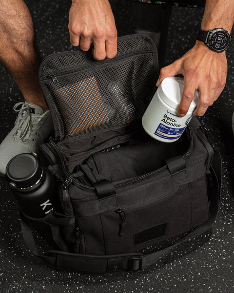Person packing KNKG mini black CORE Duffel with a supplement container and water bottle inside.