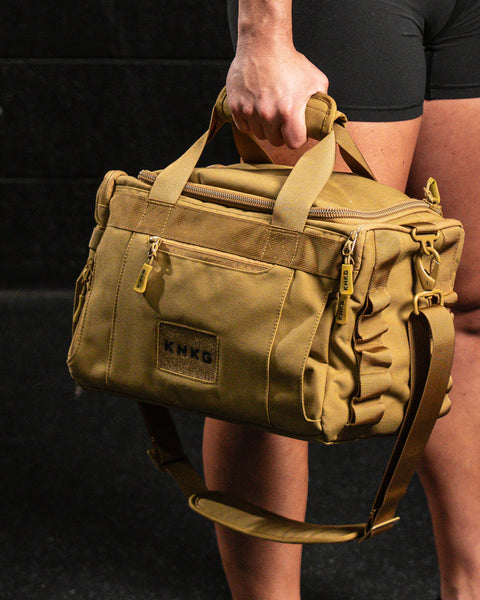 Athlete holding KNKG desert tan color mini CORE duffel by handle 
