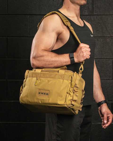 Person wearing KNKG desert tan color mini CORE duffel over shoulder in gym