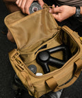 Person packing KNKG desert tan color mini CORE duffel with therragun and recovery tape