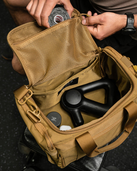 Person packing KNKG desert tan color mini CORE duffel with therragun and recovery tape