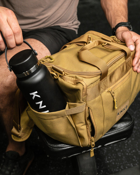 Person packing water bottle in pocket of KNKG desert tan color mini CORE duffel