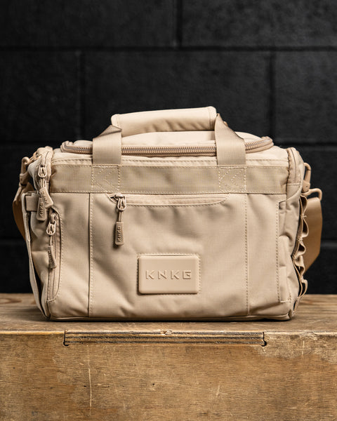 Front view of Neutral beige KNKG mini CORE Duffel sitting on wooden box
