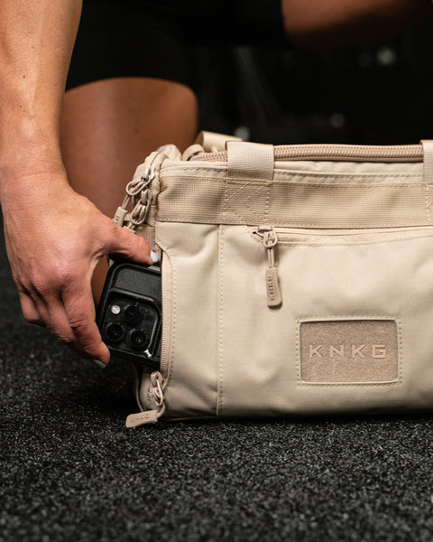 Person reaching for phone inside pocket of Neutral beige KNKG mini CORE Duffel