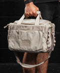 Man holding Neutral beige KNKG mini CORE Duffel by grab handle 