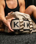 Person sitting on floor of gym reaching for lifting belt attached to Neutral beige KNKG mini CORE Duffel