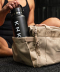 Person reaching for drink bottle inside pocket of Neutral beige KNKG mini CORE Duffel