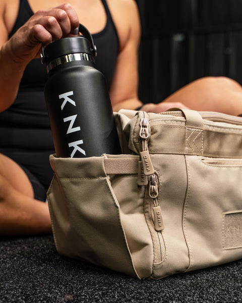 Person reaching for drink bottle inside pocket of Neutral beige KNKG mini CORE Duffel