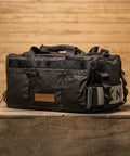 Side view of KNKG Waxed Canvas Duffel  sitting on box with matching lifting belt attached 