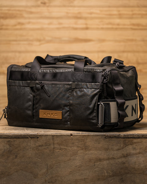 Side view of KNKG Waxed Canvas Duffel  sitting on box with matching lifting belt attached 
