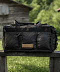 KNKG Waxed Canvas Duffel sitting on wooden bench in front of wooden barn