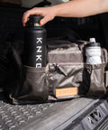 Person putting drink bottle in front pocket of KNKG Waxed Canvas Duffel 