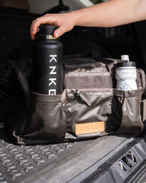 Person putting drink bottle in front pocket of KNKG Waxed Canvas Duffel 
