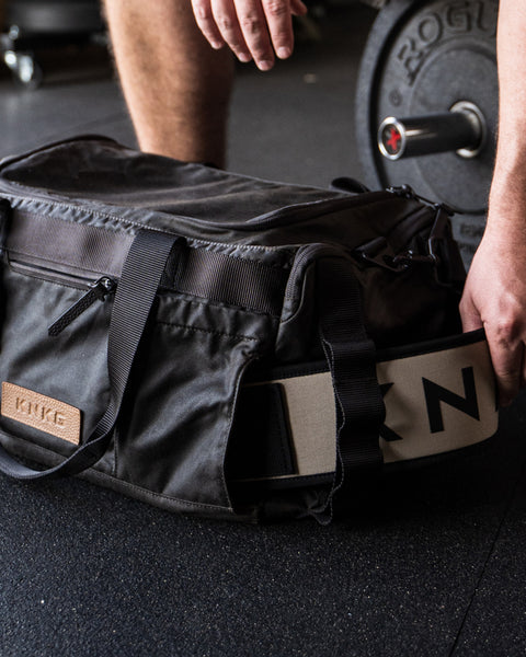 Close up of person pulling weightlifting belt out of KNKG Waxed Canvas Duffel 