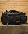 KNKG Waxed Canvas Duffel sitting on wooden box inside barn style gym