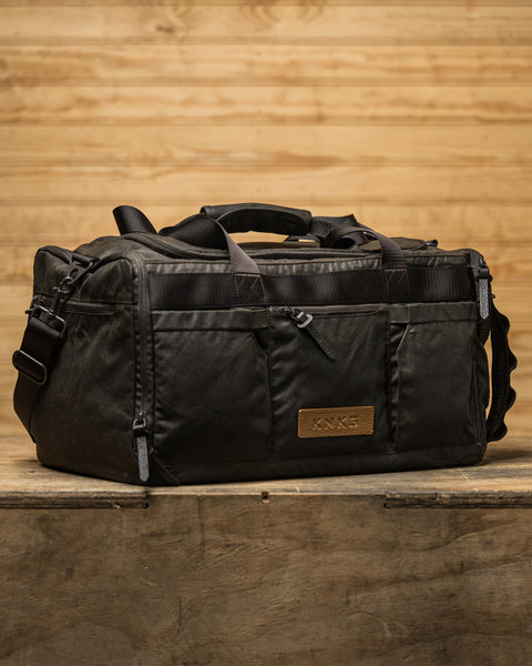 KNKG Waxed Canvas Duffel sitting on wooden box inside barn style gym