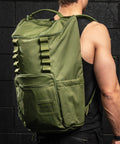 Man standing against black brick wall, wearing large green CORE Backpack