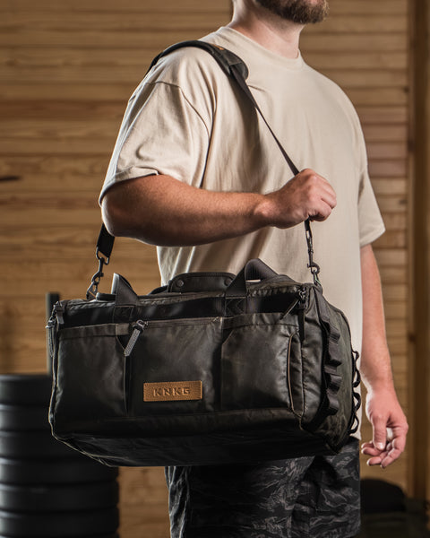 Athlete wearing KNKG Waxed Canvas Duffel over shoulder in barn style gym